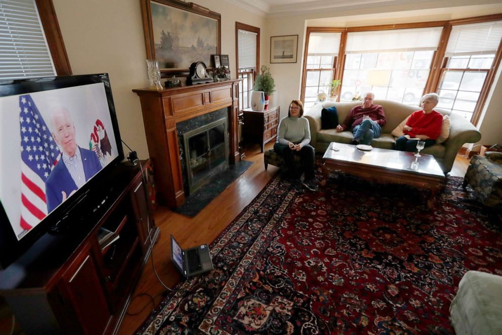 PHOTO: Lally Doerrer, left, and neighbors Douglas and Marlene Groll, watch Joe Biden during his Illinois virtual town hall, in her living room Friday, March 13, 2020, in Chicago.