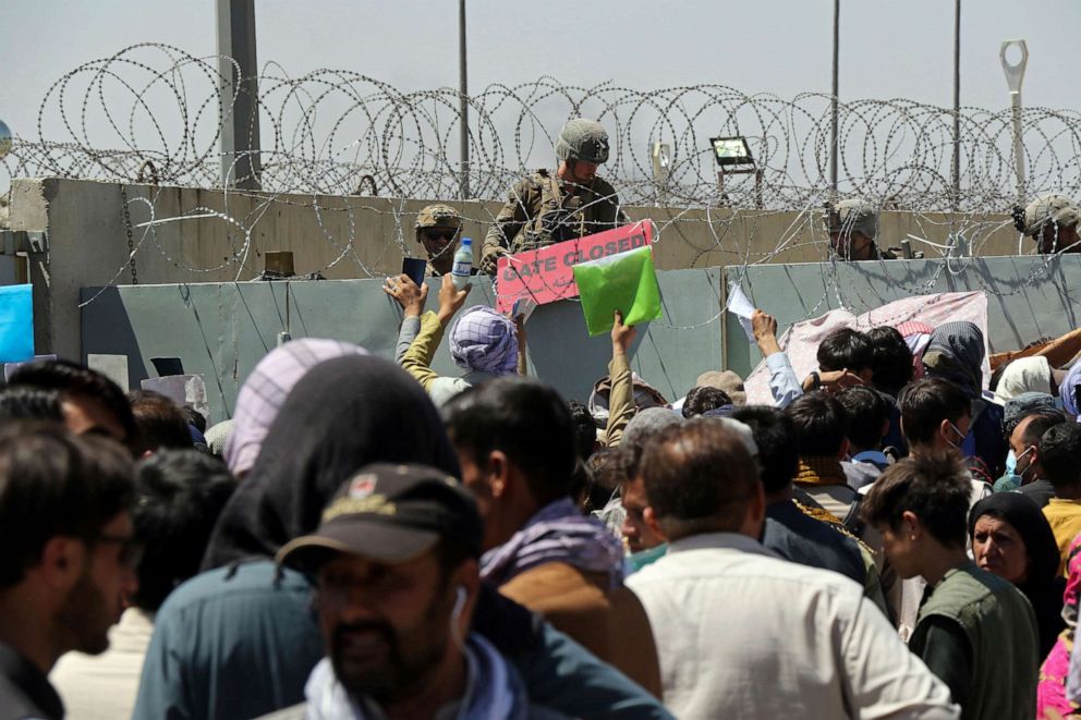 PHOTO: A U.S. soldier holds a sign indicating a gate is closed as hundreds of people gather some holding documents, near an evacuation control checkpoint on the perimeter of the Hamid Karzai International Airport, in Kabul, Afghanistan, Aug. 26, 2021.