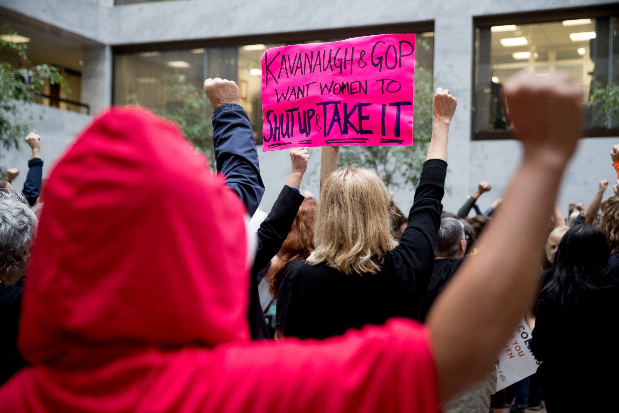 A protester of Supreme Court nominee Brett Kavanaugh wears a costume from the show "The Handmaid's Tale," and another protester holds up a sign that reads "Kavanaugh and GOP Want Women to Shut Up and Take It" in Washington, Monday, Sept. 24, 2018.
