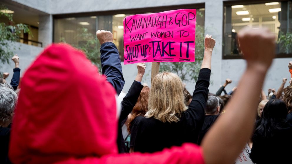 A protester of Supreme Court nominee Brett Kavanaugh wears a costume from the show "The Handmaid's Tale," and another protester holds up a sign that reads "Kavanaugh and GOP Want Women to Shut Up and Take It" in Washington, Monday, Sept. 24, 2018.