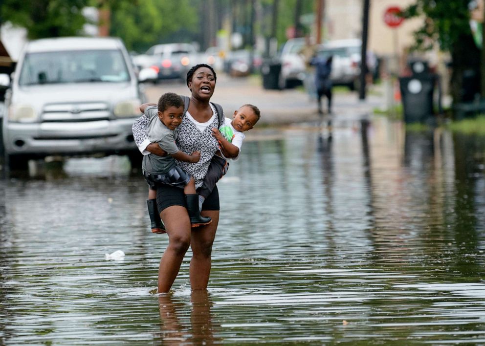 PHOTO: A woman carries two children through rising waters in New Orleans, July 10, 2019, during flooding from a storm in the Gulf Mexico.