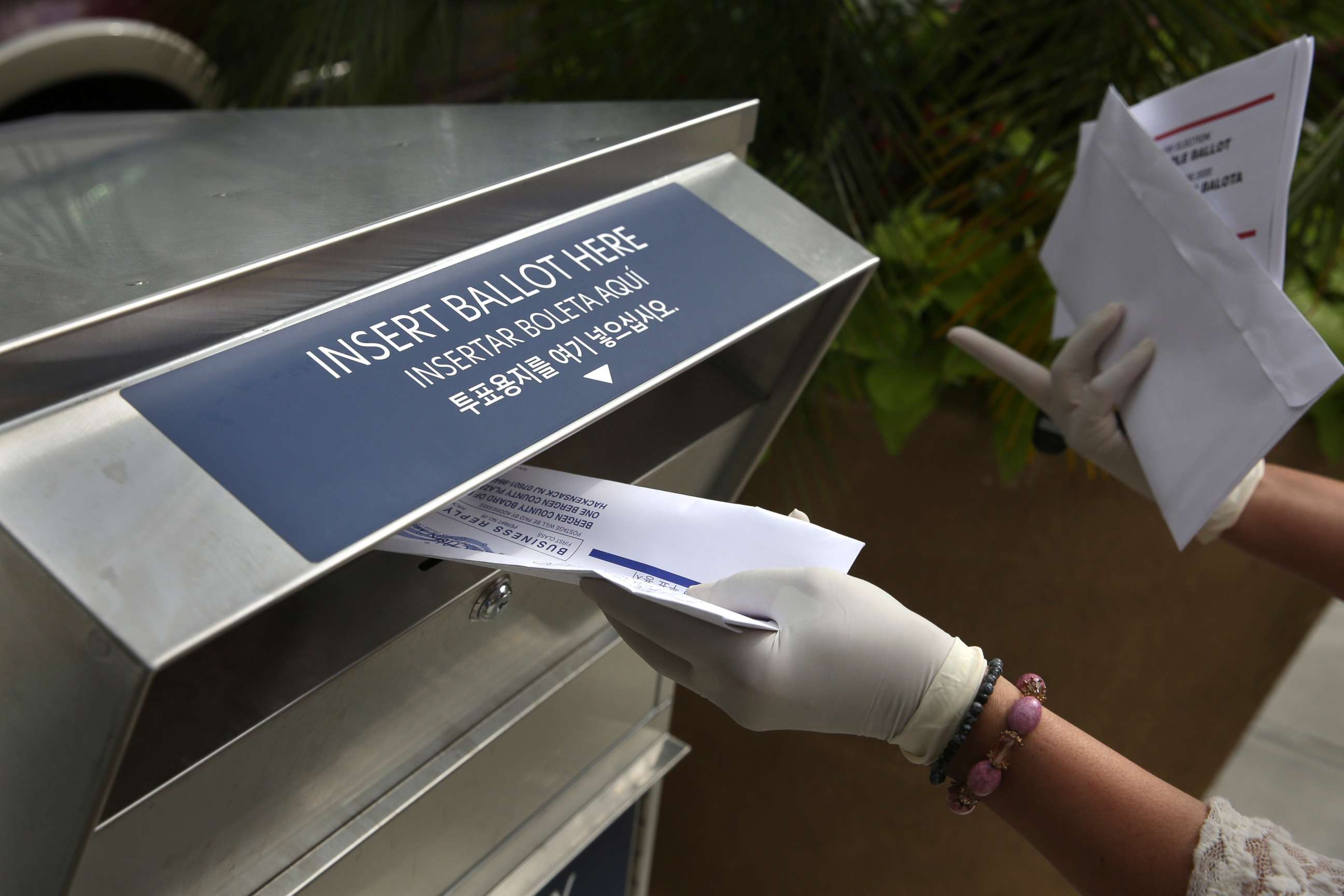 PHOTO: In this July 7, 2020, file photo a woman wearing gloves drops off a mail-in ballot at a drop box in Hackensack, N.J.