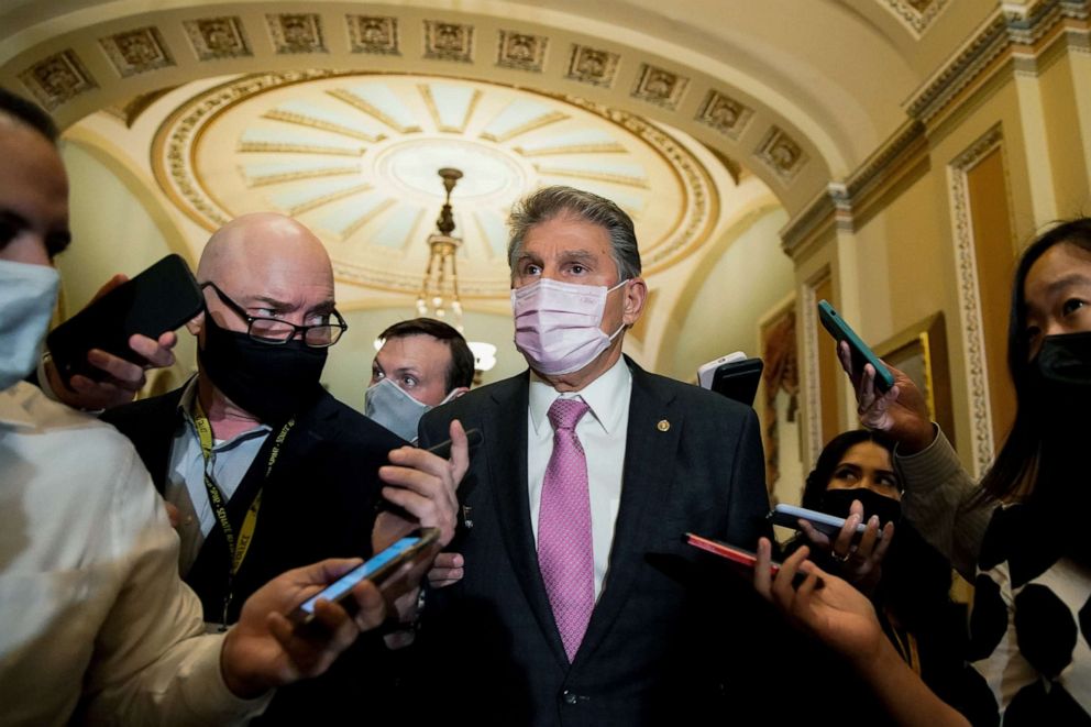 PHOTO: Sen. Joe Manchin walks through a hallway as reporters ask questions following the Senate Democrats weekly policy lunch at the Capitol, Oct. 19, 2021. 