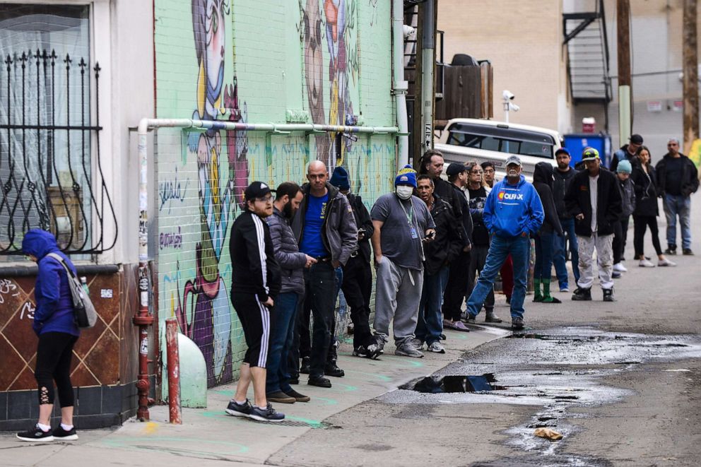 PHOTO: In this March 23, 2020, file photo, people stand in freshly painted circles, six-feet-apart, as they wait in a two-hour line to buy marijuana products from Good Chemistry in Denver.