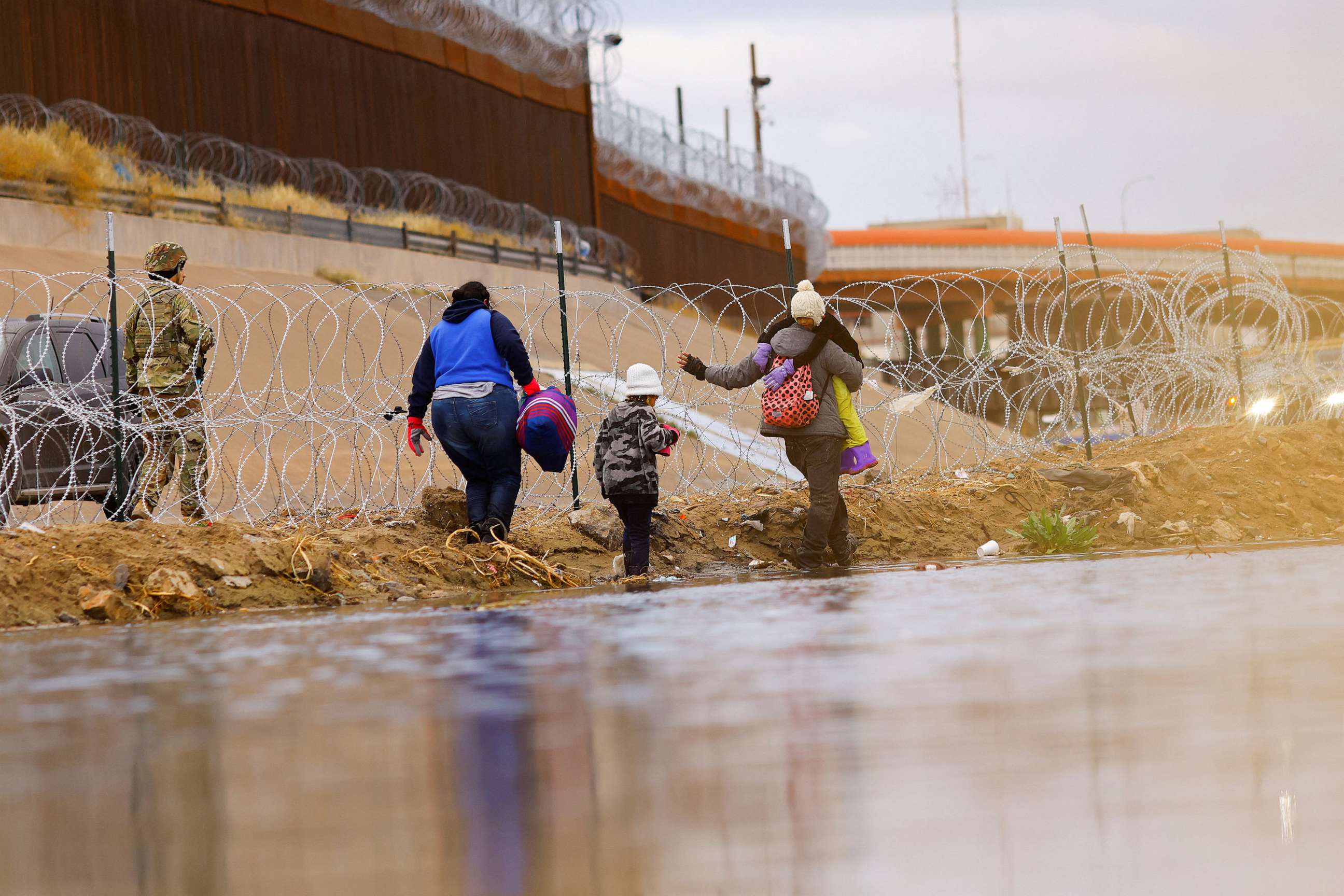 PHOTO: In this Jan. 17, 2023, file photo, asylum-seeking migrants walk past a razor wire fence as members of the Texas National Guard stand guard on the banks of the Rio Bravo river, as seen from Ciudad Juarez, Mexico.