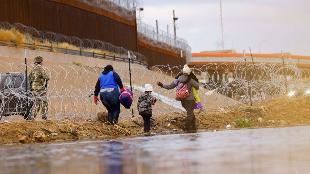 PHOTO: In this Jan. 17, 2023, file photo, asylum-seeking migrants walk past a razor wire fence as members of the Texas National Guard stand guard on the banks of the Rio Bravo river, as seen from Ciudad Juarez, Mexico.