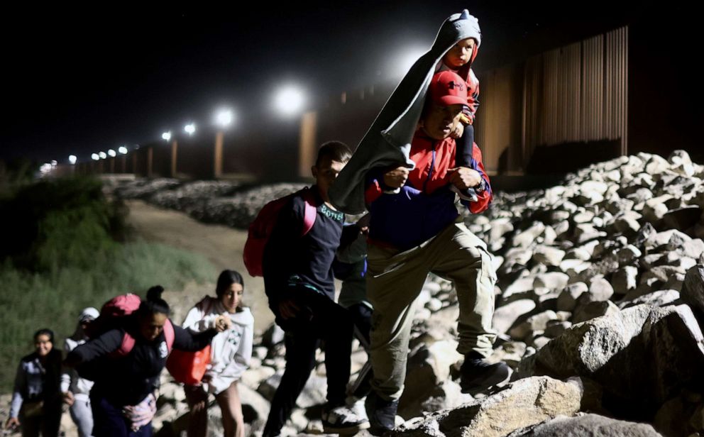 PHOTO: Immigrants seeking asylum in the United States walk along the border fence on their way to be processed by U.S. Border Patrol agents in the early morning hours after crossing into Arizona from Mexico on May 11, 2023 in Yuma, Ariz.