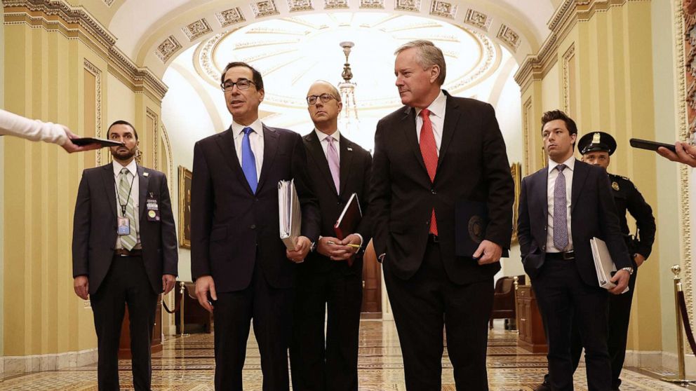 PHOTO: Treasury Secretary Steven Mnuchin talks briefly with reporters after arriving at the Capitol with White House Director of Legislative Affairs Eric Ueland and White House Chief of Staff Mark Meadows, March 24, 2020 in Washington.