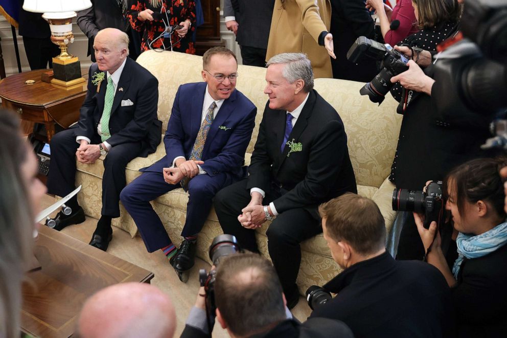 PHOTO: White House Chief of Staff Mark Meadows, right, talks with his predecessor, Mick Mulvaney, center, as Edward Crawford, U.S. Ambassador to Ireland, left, attends a meeting in the Oval Office at the White House, March 12, 2020, with President Trump.