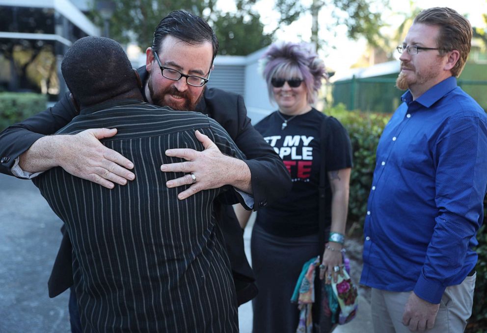 PHOTO: Neil Volz is hugged by Permon Thomas as he and Lance Wissinger, right, arrive to fill out a voter registration form at the Lee Country Supervisor of Elections office, Jan. 8, 2019 in Fort Myers, Fla.