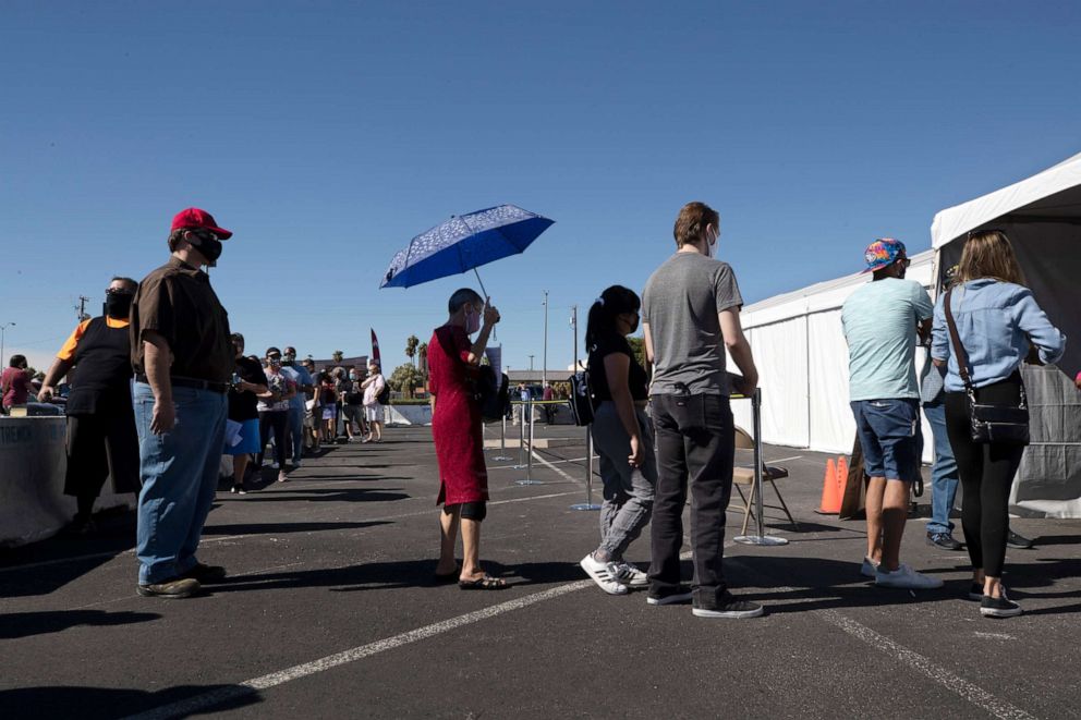 PHOTO: In this Oct. 17, 2020 file photo a woman uses an umbrella for shade as voters line up at an early voting site during the first day of early voting in Las Vegas. 
