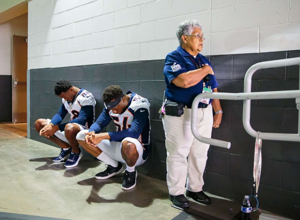 PHOTO: A stadium security guard stands with her hand over her heart as Denver Broncos linebacker Brandon Marshall (54) and wide receiver Demaryius Thomas (88) sit in silent protest during the national anthem prior a game, Aug. 30, 2018 in Glendale, Ariz.