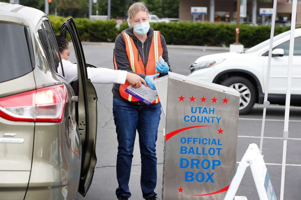 PHOTO: A women is helped by an election worker to put her ballot in a box while voting from her car in the parking lot of Lavell Edwards Stadium on the campus of Brigham Young University, June 30, 2020, in Provo, Utah. 