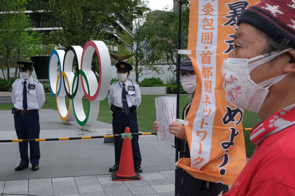 PHOTO: Security guards keep watch next to the Olympic Rings while people take part in a protest against the hosting of the 2020 Tokyo Olympic Games, in front of the headquarters building of the Japanese Olympic Committee in Tokyo, May 18, 2021.