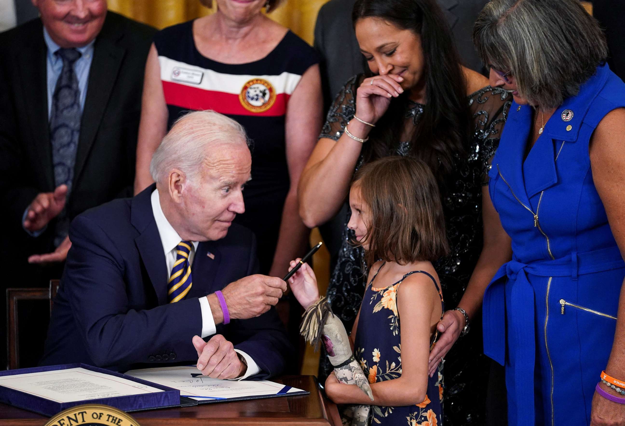 PHOTO: President Joe Biden hands a pen to Brielle Robinson, the daughter of Sgt. 1st Class Heath Robinson, as her mother, Danielle Robinson, stands by during a signing ceremony for PACT Act of 2022, in the East Room of the White House, Aug. 10, 2022.