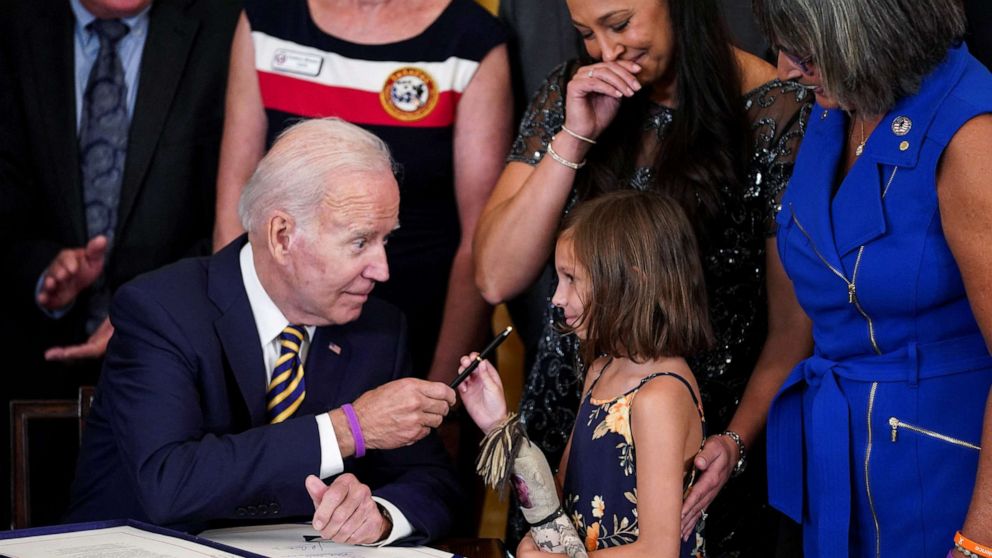 PHOTO: President Joe Biden hands a pen to Brielle Robinson, the daughter of Sgt. 1st Class Heath Robinson, as her mother, Danielle Robinson, stands by during a signing ceremony for PACT Act of 2022, in the East Room of the White House, Aug. 10, 2022.