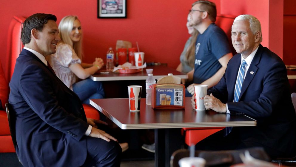 PHOTO: Vice President Mike Pence, right, talks to Florida Gov. Ron DeSantis as they wait for their lunch at Beth's Burger Bar, May 20, 2020, in Orlando, Fla. 