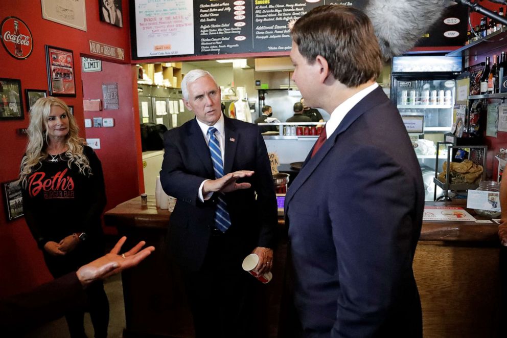 PHOTO: Vice President Mike Pence, center, gestures as he speaks to Florida Gov. Ron DeSantis, right, after ordering lunch at Beth's Burger Bar, May 20, 2020, in Orlando, Fla.