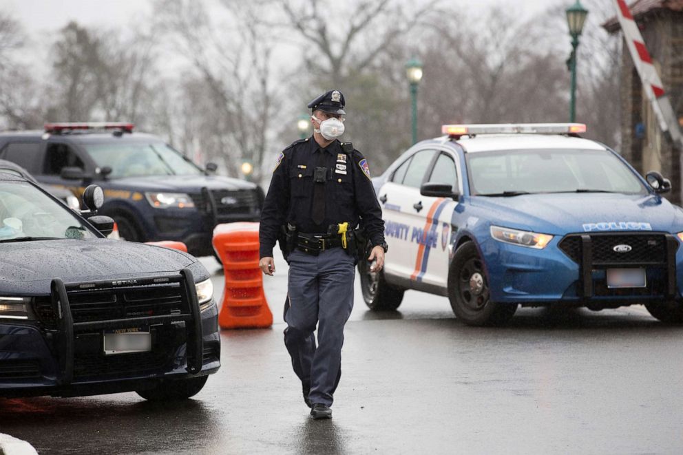 PHOTO: A police officer wears a protective mask maintains a road block on the bridge leading to a six lane coronavirus drive-through testing facility at Glen Island Park in New Rochelle, N.Y., March 13, 2020. 