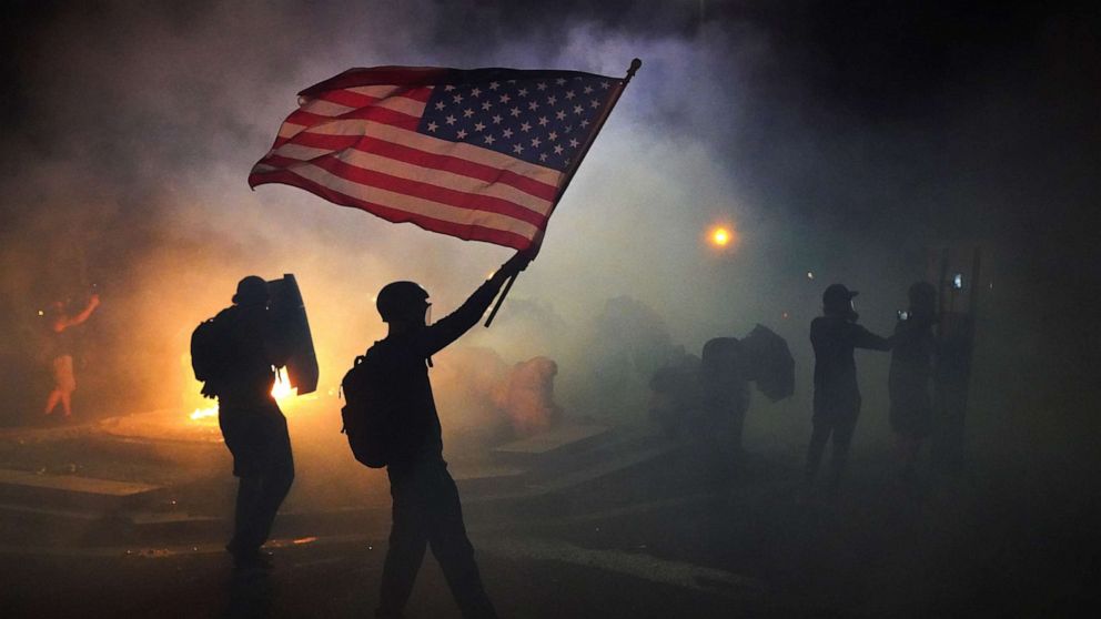 PHOTO: A protester flies an American flag while walking through tear gas fired by federal officers during a protest in front of the Mark O. Hatfield U.S. Courthouse, July 21, 2020, in Portland, Ore. 