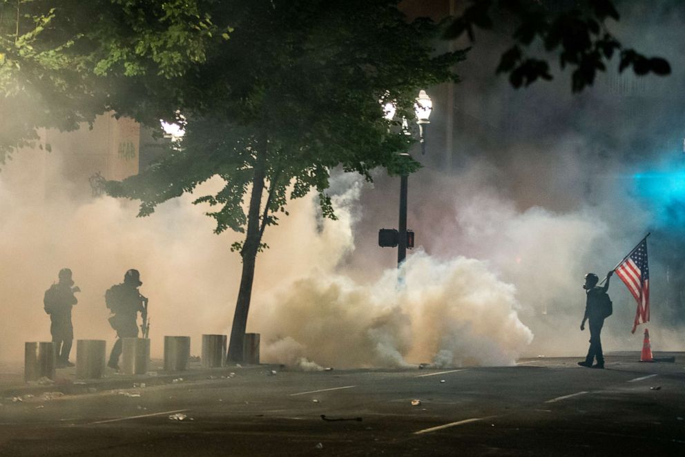 PHOTO: Federal officers, left, and a protester carrying the American flag face off in front of the Mark O. Hatfield U.S. Courthouse on July 21, 2020 in Portland, Ore.