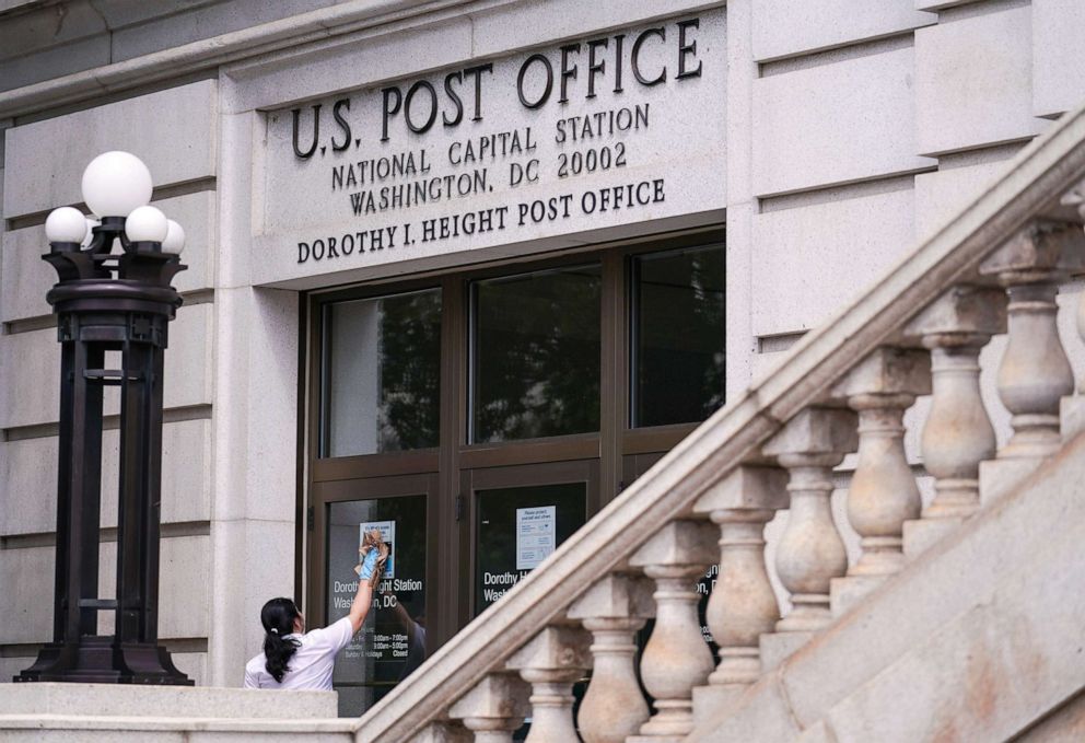 PHOTO: A woman cleans the doors of the National Capital Station U.S. Post Office near Capitol Hill in Washington, D.C., Aug. 13, 2020.