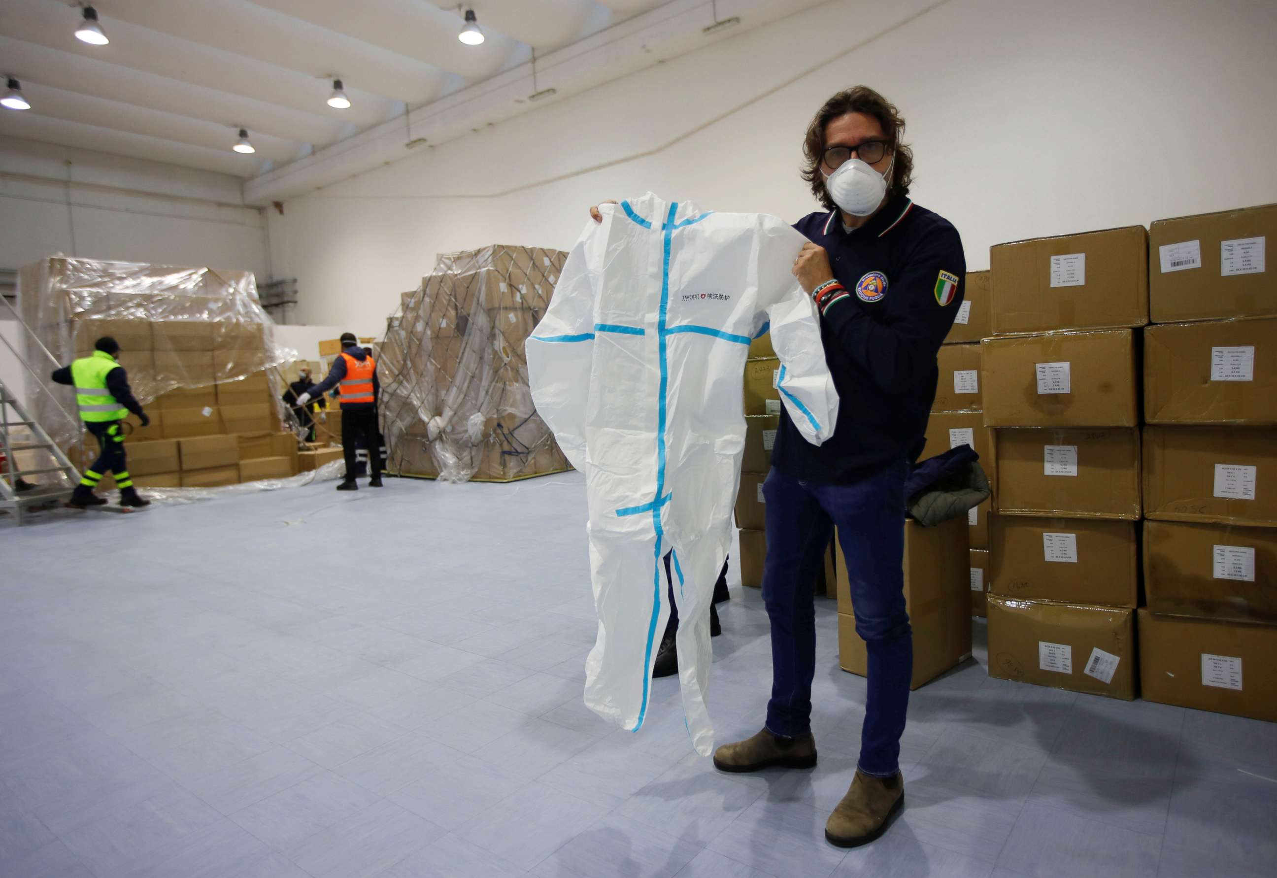 PHOTO: A member of the Italian Civil Protection shows a protective suit that came in a shipment containing supplies of personal protective equipment in Bari, Italy, April 7, 2020.