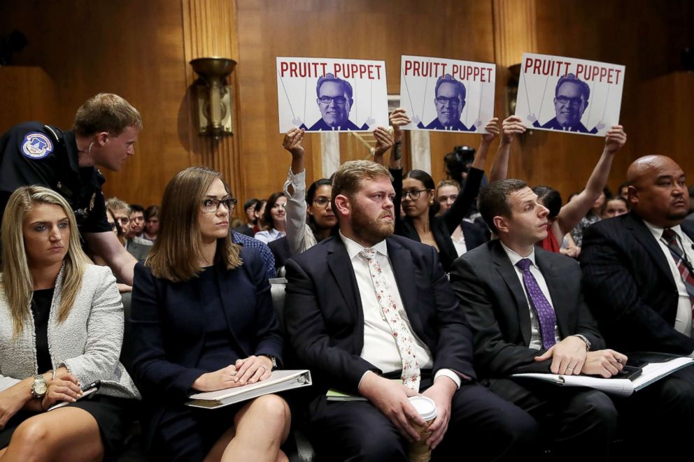 PHOTO: Protesters hold up signs during the testimony of Acting EPA Administrator Andrew Wheeler before the Senate Environment and Public Works Committee, Aug. 1, 2018, in Washington, DC.