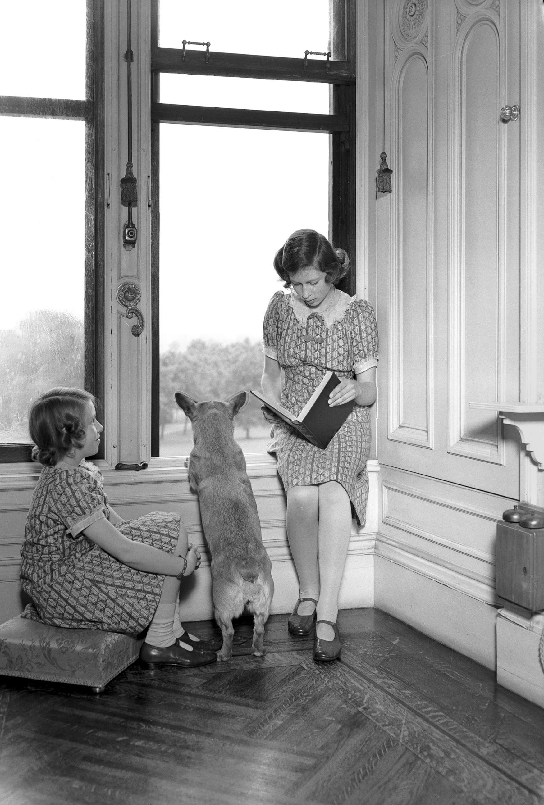 PHOTO: Princess Margaret, left, and Princess Elizabeth read together, while a Corgi peers out of a window at Windsor Castle, June 22, 1940.
