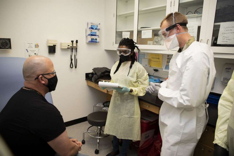 PHOTO: Cpt. Aaron Sanborn, RN, (far right), discusses the vaccination process with Francis Holinaty (left) during the first day of the vaccine entering clinical trials at the Walter Reed Army Institute of Research's Clinical Trials Center, April 6, 2021.