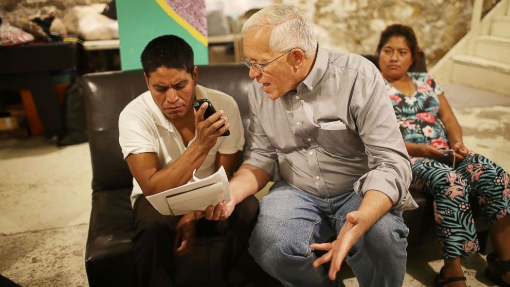 Ruben Garcia (C), director of the Annunciation House, speaks on a cell phone with a person from the Office of Refugee Resettlement as he sits with Cristian, who migrated from Guatemala, and Miriam, who migrated from Honduras as they try to track down their children after being released from U.S. Customs and Border Protection custody, June 25, 2018, in El Paso, Texas. Cristian and Miriam are part of a group of 32 parents that arrived at the Annunciation House migrant shelter as they wait to be reunited with their children.