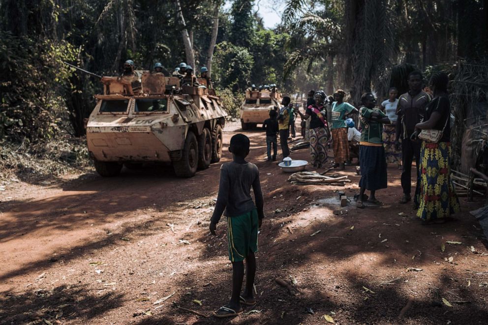 Families displaced from a conflict watch as a convoy of Moroccan peacekeepers from the United Nations Integrated Multidimensional Stabilization Mission in the Central African Republic (MINUSCA) passes by on the outskirts of Bangassou on Feb. 3, 2021.
