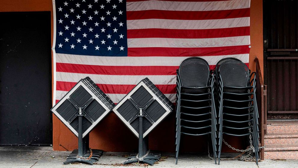 PHOTO: Chairs and tables are stacked in front of an American flag at a closed restaurant, April 27, 2020 in New York.