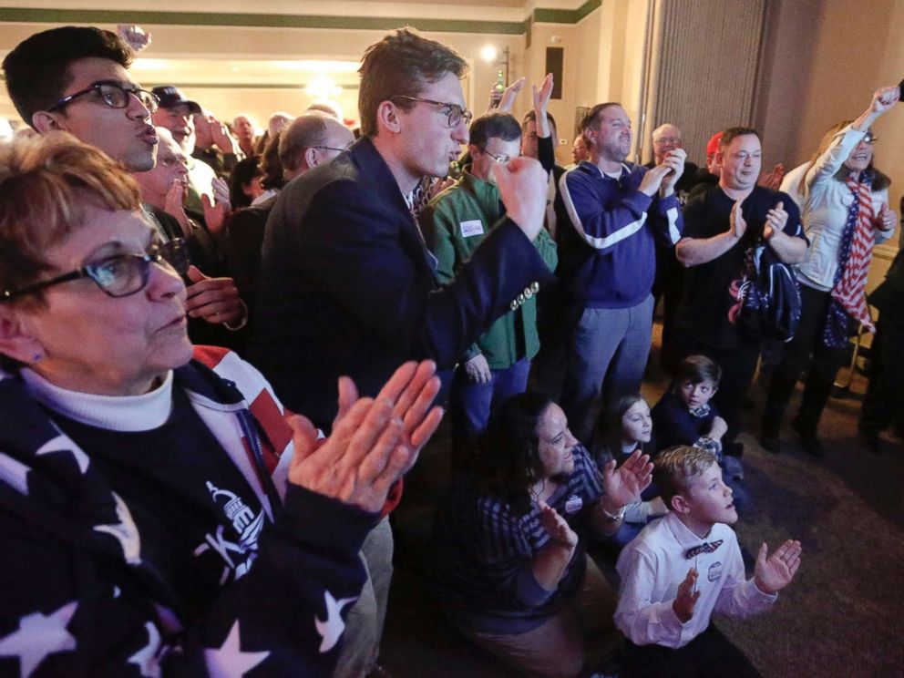 PHOTO: Bobbi Bauer, left, Khalid Husain, top, and Demetrios Germanos, center, celebrate with the crowd as results on the television say Republican Rick Saccone was closing the gap to under 1 percent of the vote March 13, 2018, in McKeesport, Pa.