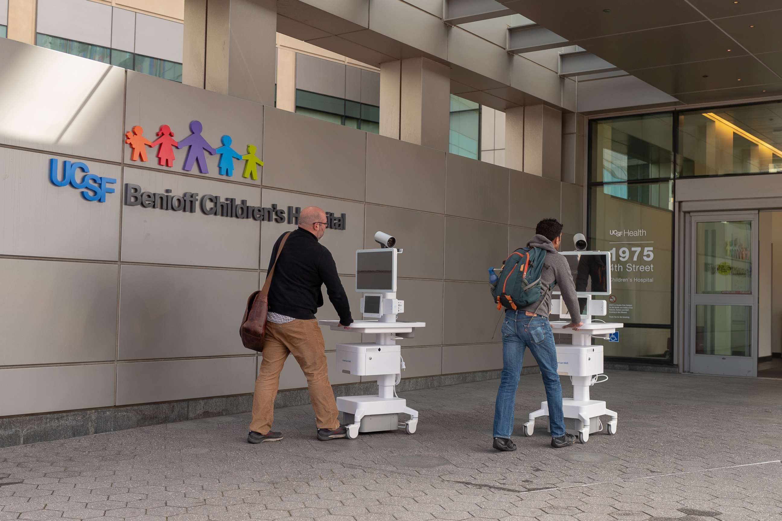 PHOTO: Two staff members wheel Amwell telemedicine carts into the entrance of the University of California San Francisco Benioff Children's Hospital during an outbreak of the COVID-19 coronavirus, March 16, 2020.