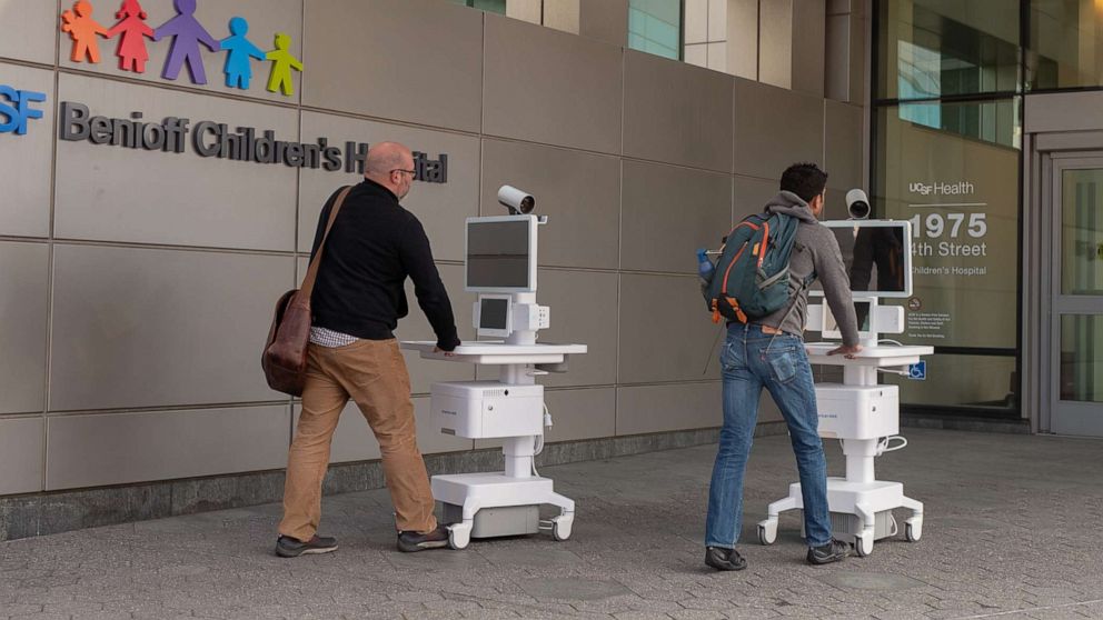 PHOTO: Two staff members wheel Amwell telemedicine carts into the entrance of the University of California San Francisco Benioff Children's Hospital during an outbreak of the COVID-19 coronavirus, March 16, 2020.