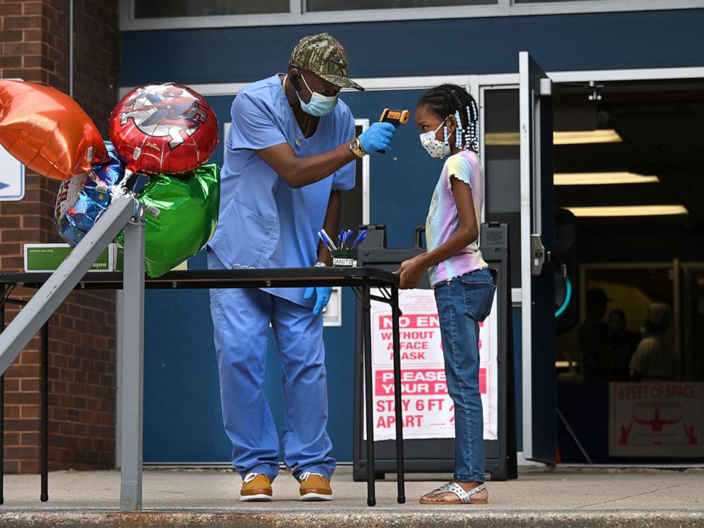 PHOTO: Keith Boyd a former special education teacher who is volunteering at Bernard Harris Elementary School to help with summer school, takes the temperature of Kennedy Harris, a second grader, before she can enter the school.