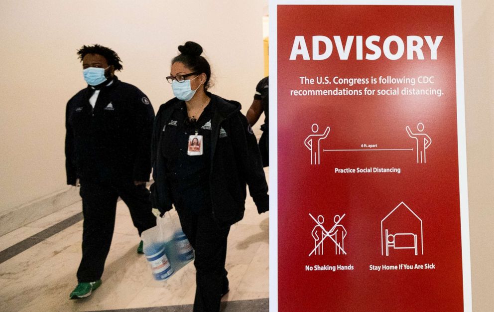 PHOTO: Architect of the Capitol workers wearing face masks walk past a sign advising people observe social distancing in the Russell Senate Office Building on Monday, May 4, 2020., in Washington.
