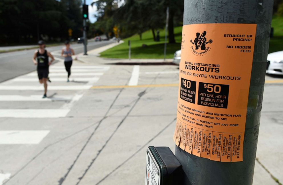 PHOTO: Joggers run past an ad for online "social distancing" workouts, March 24, 2020, at Griffith Park in Los Angeles.