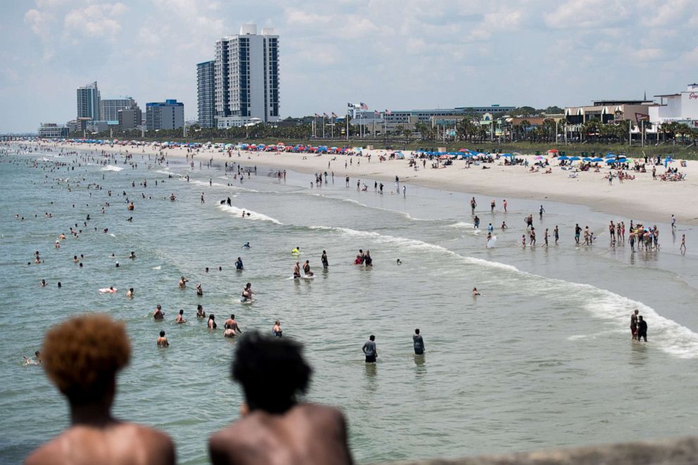 PHOTO: Two young men watch as people wade in the ocean, July 4, 2020, in Myrtle Beach, S.C. 