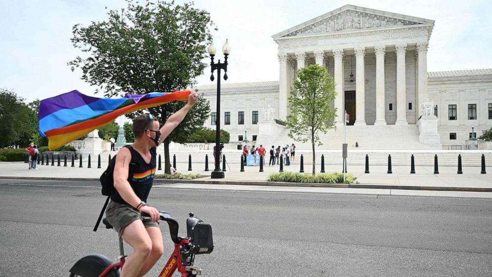 PHOTO: A man waves a rainbow flag as he rides by the US Supreme Court that released a decision that says federal law protects LGBTQ workers from discrimination, June 15, 2020, in Washington,DC.