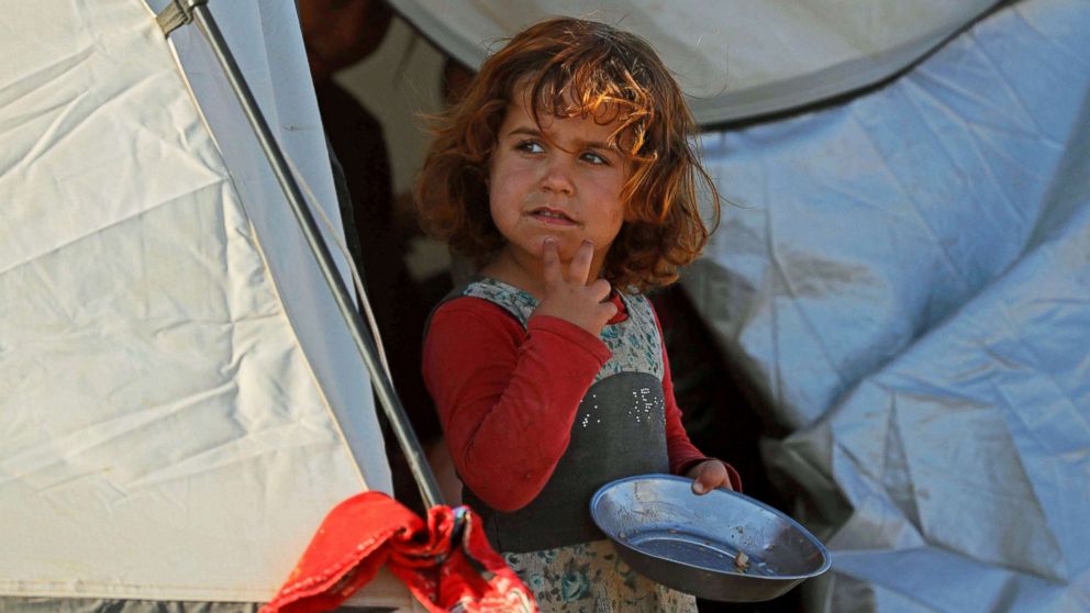 A girl holds an empty metal plate inside a refugee camp for people displaced by fighting between the Syrian Democratic Forces and Islamic State militants in Ain Issa, Syria, Oct. 3, 2017. 