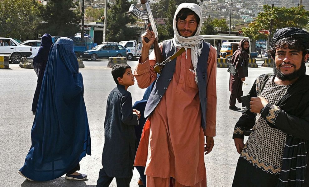 PHOTO: Commuters walk past Taliban fighters outside the Kabul Governor Building in Kabul, Afghanistan, Oct. 3, 2021.