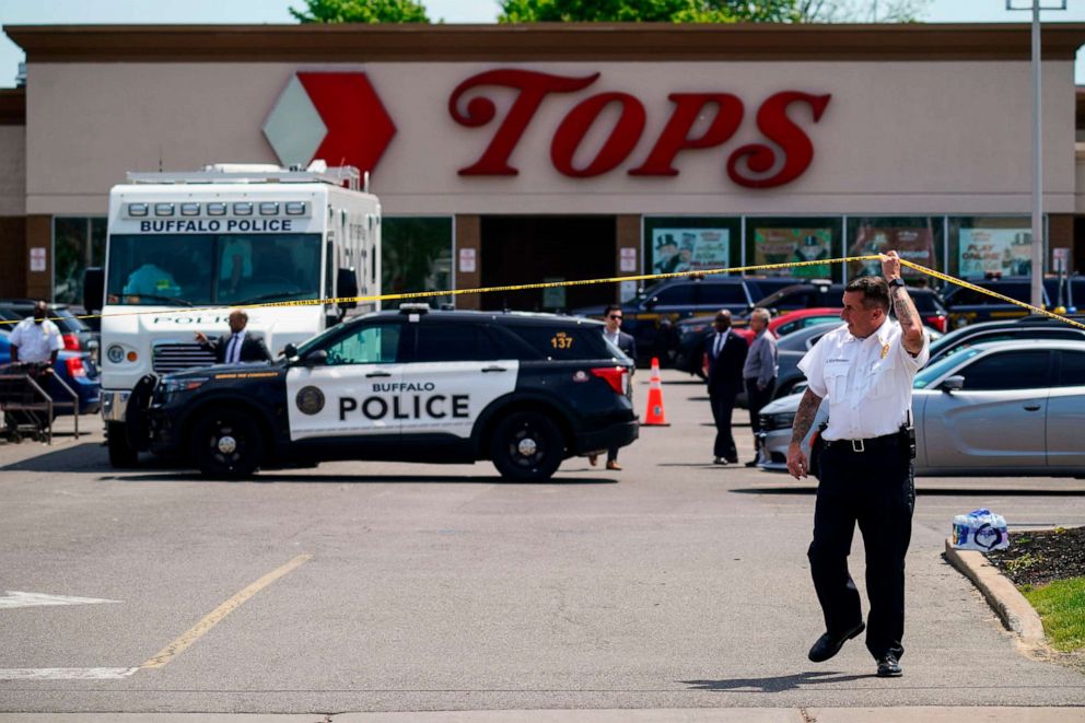 PHOTO: A police officer lifts the tape cordoning off the scene of a shooting at a supermarket, in Buffalo, NY, May 15, 2022.