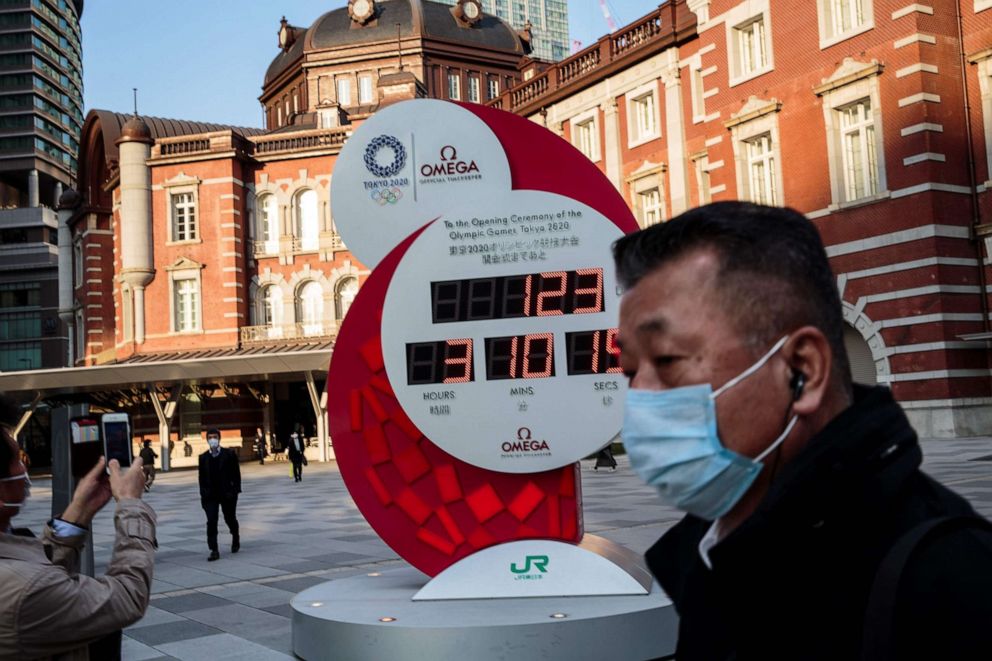 PHOTO: A man wearing a face mask amid concerns over the spread of the COVID-19 coronavirus walks past the Olympic countdown clock outside Tokyo station on March 23, 2020.
