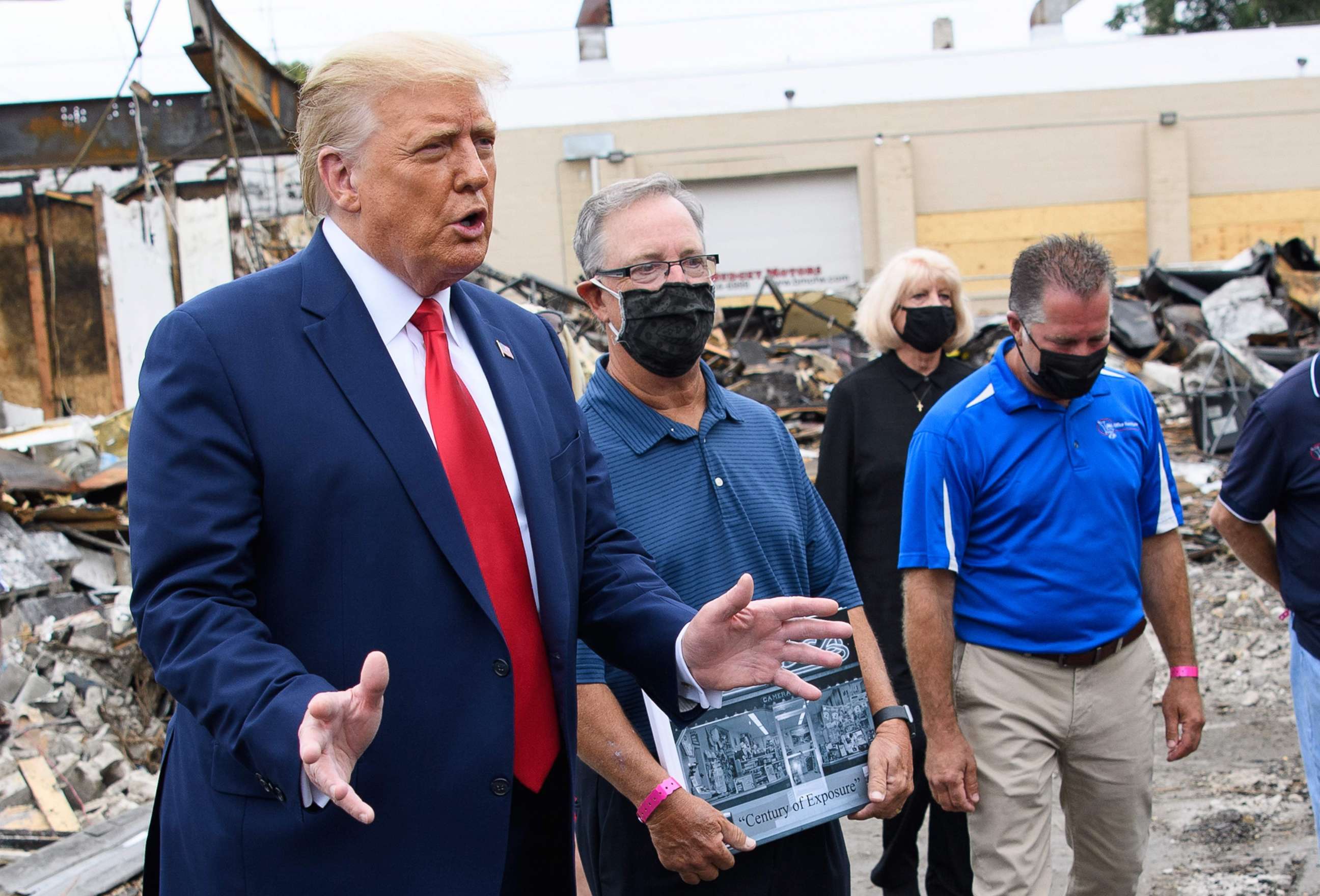 PHOTO: President Donald Trump speaks to the press as he tours an area affected by civil unrest in Kenosha, Wis., Sept. 1, 2020, as John Rode(C), the former owner of Rode's Camera Shop looks on holding a sign.