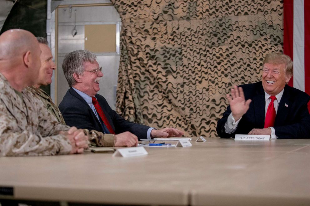 PHOTO: In this Dec. 26, 2018, file photo, President Donald Trump, right, jokes with National Security Adviser John Bolton, third from left, and senior military leadership, as he speaks to members of the media at Al Asad Air Base, Iraq.