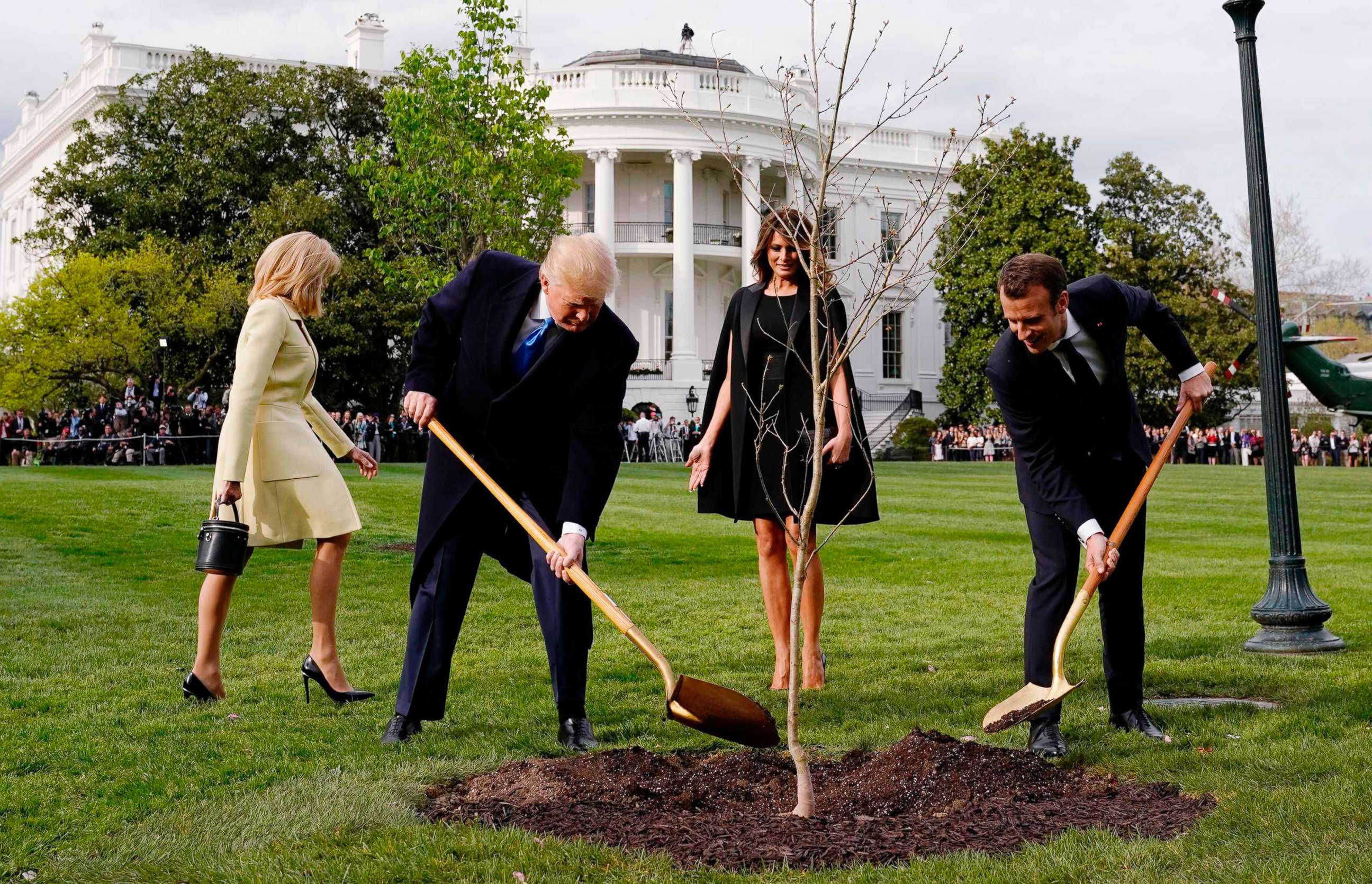 PHOTO: President Donald Trump and French President Emmanuel Macron shovel dirt onto a freshly planted oak tree as first lady Melania Trump and Brigitte Macron watch on the South Lawn of the White House in Washington, D.C., April 23, 2018.