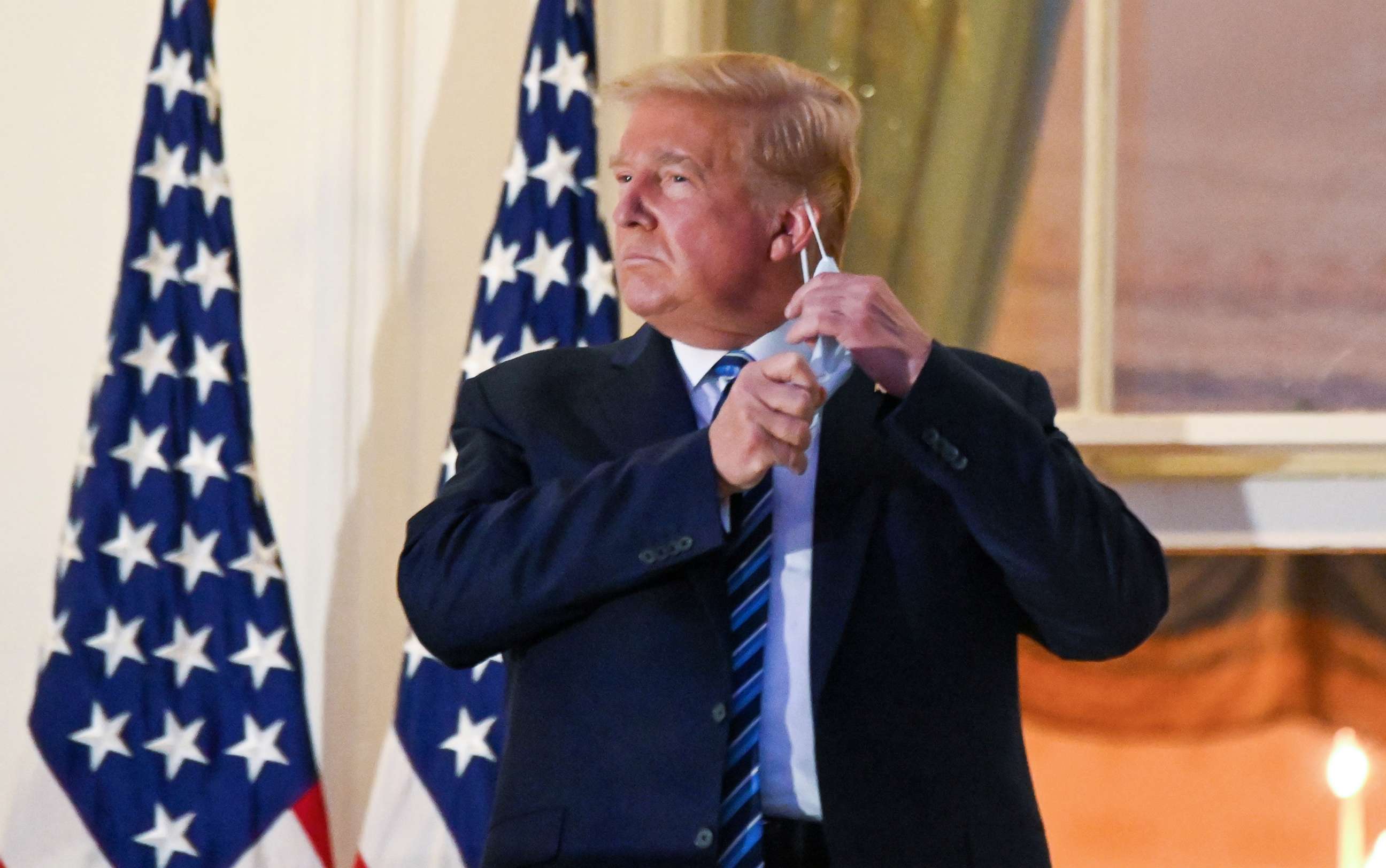 PHOTO: President Donald Trump pulls off his protective face mask as he poses atop the Truman Balcony of the White House after returning from being hospitalized at Walter Reed Medical Center for coronavirus disease (COVID-19) treatment, Oct. 5, 2020.