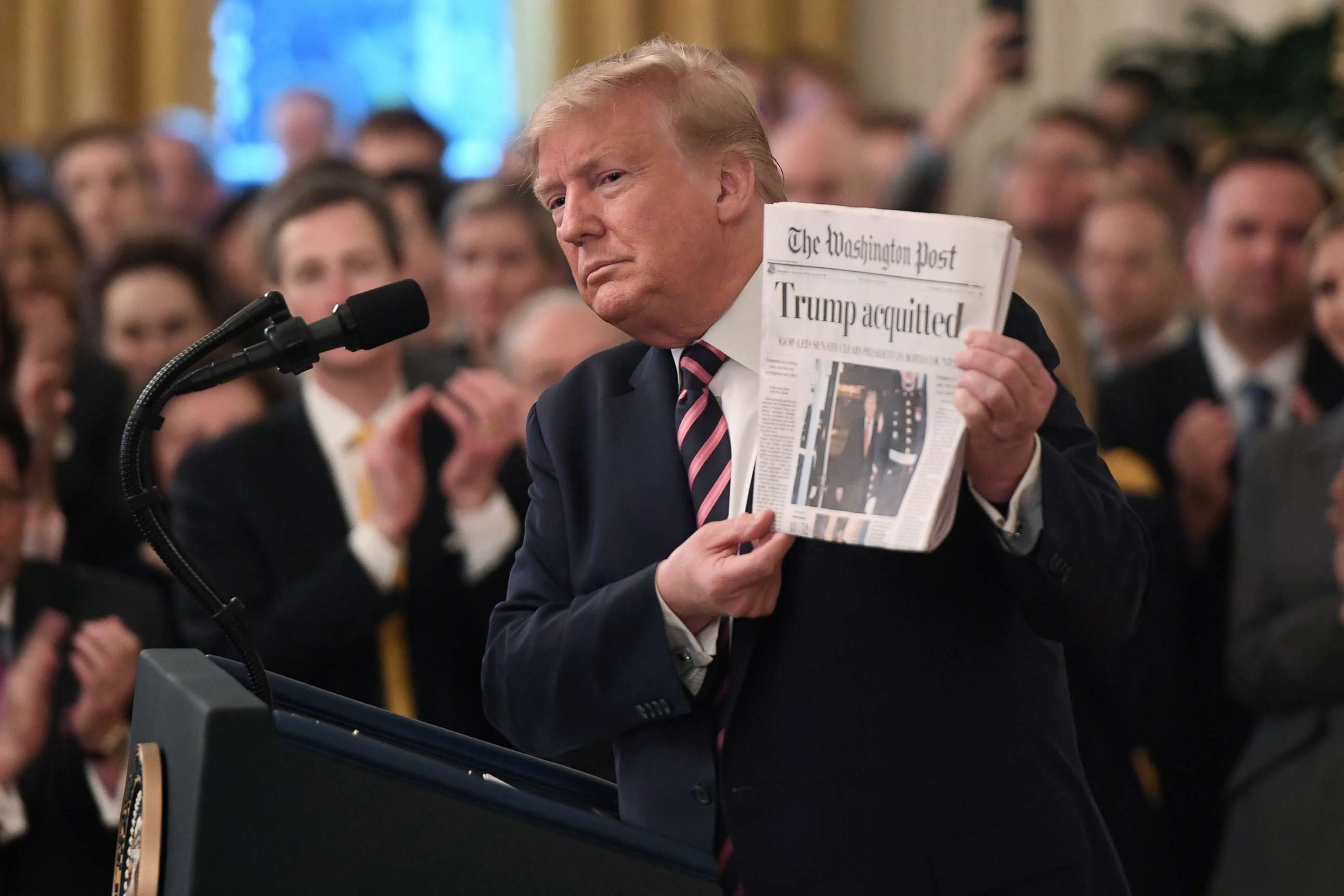 PHOTO: President Donald Trump holds up a newspaper that displays a headline "Acquitted"  while peaking about his Senate impeachment trial in the East Room of the White House, Feb. 6, 2020.